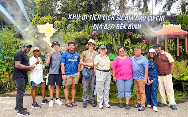 Tourists posing at Cu Chi Tunnels entrance, Vietnam, with lush greenery and signage in the background.