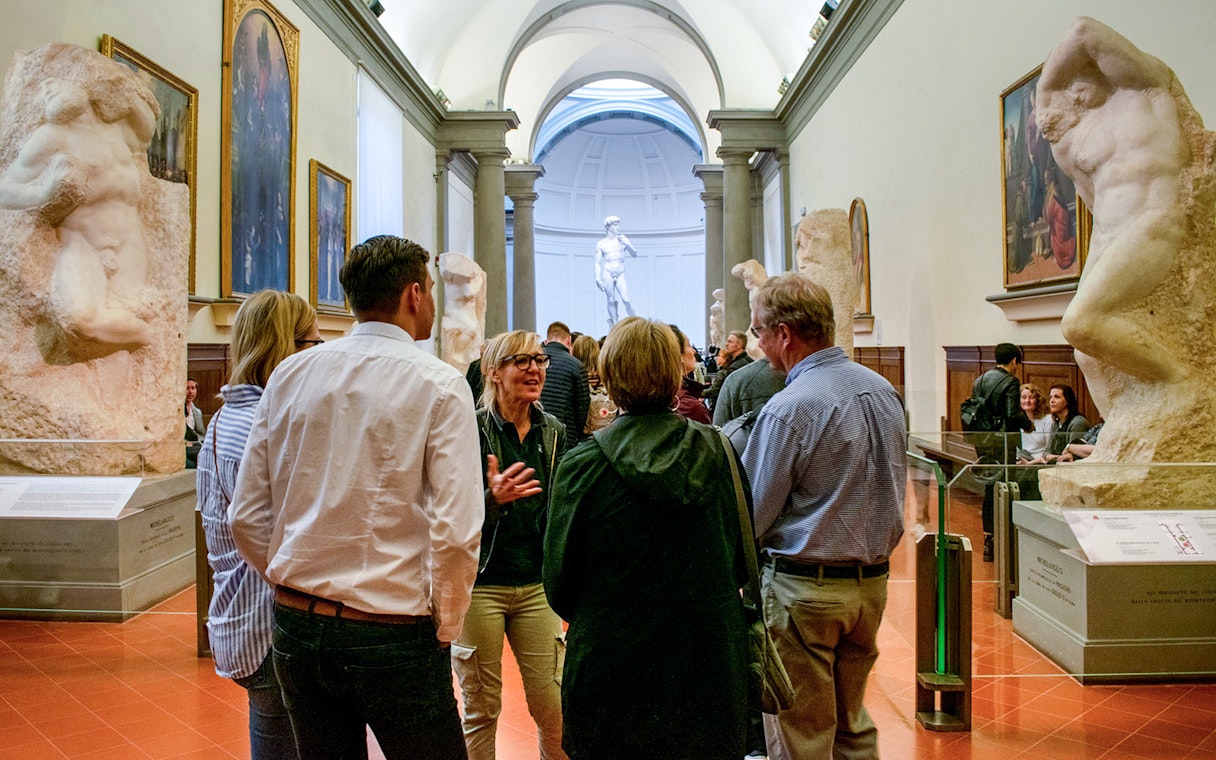 Guide leading tourists through Gallerie dell'Accademia, Florence, with sculptures in view.