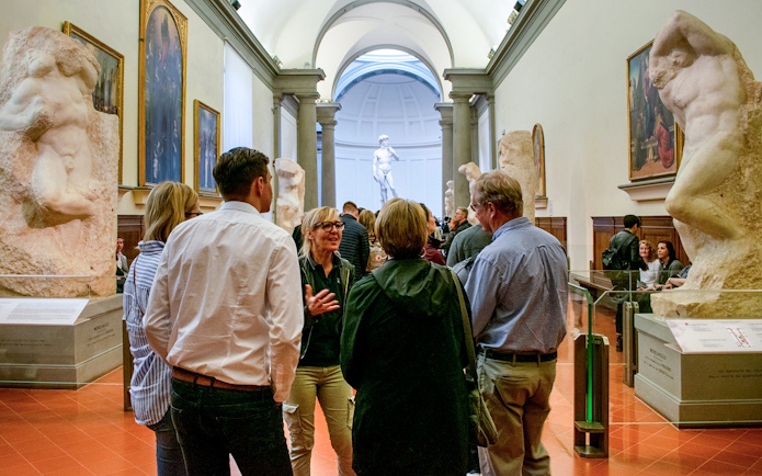 Guide leading tourists through Gallerie dell'Accademia, Florence, with sculptures in view.