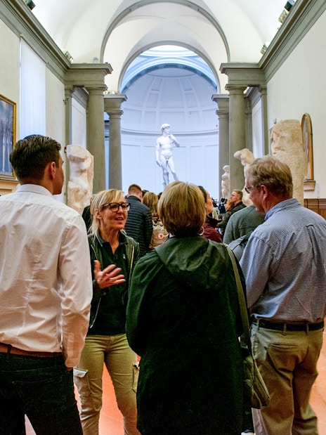 Guide leading tourists through Gallerie dell'Accademia, Florence, with sculptures in view.