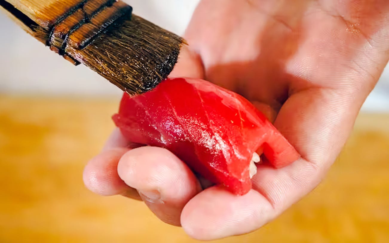 Nigiri sushi being brushed with sauce in a hand.