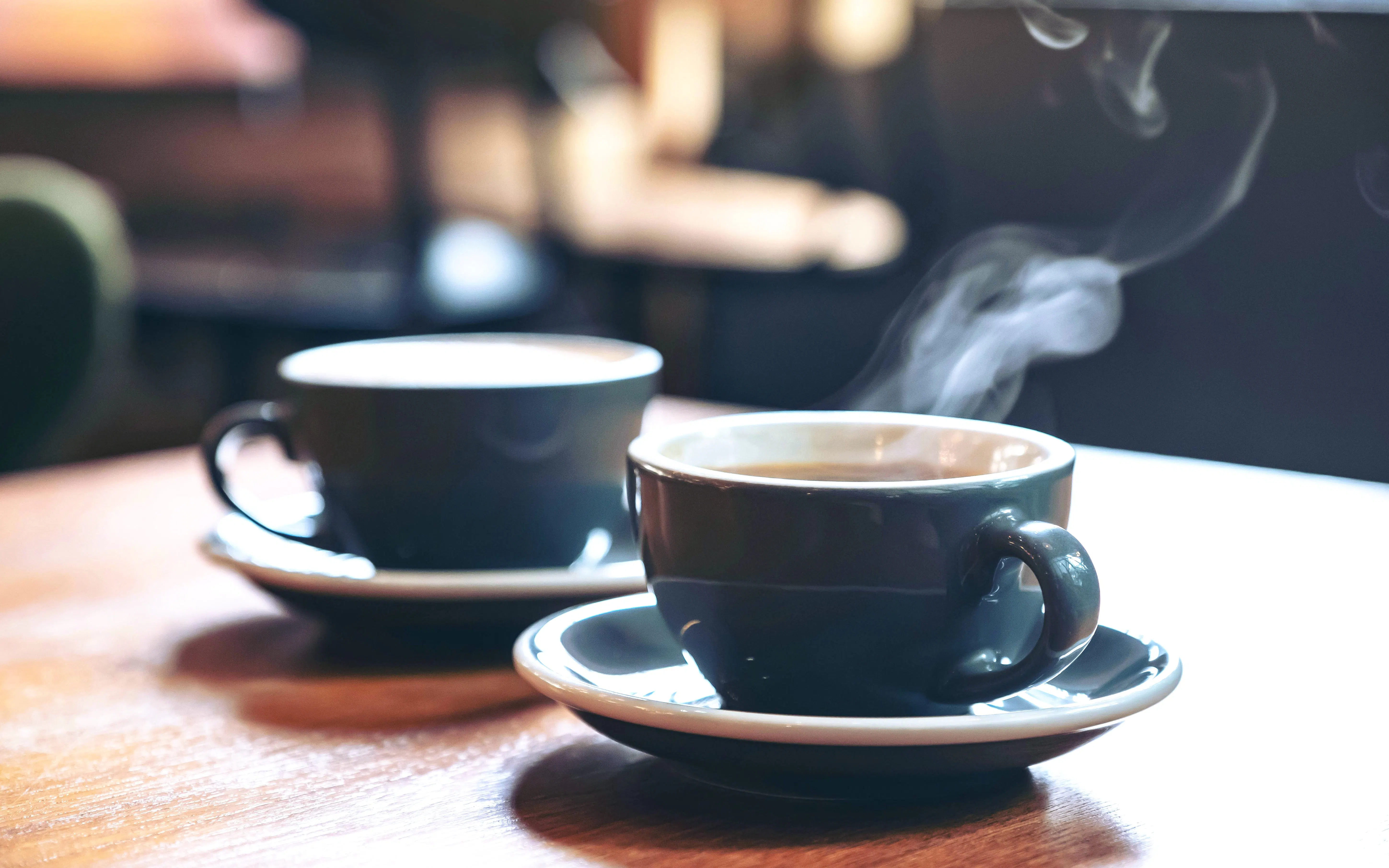 Two blue cups of steaming latte and Americano on a wooden table in a cafe.