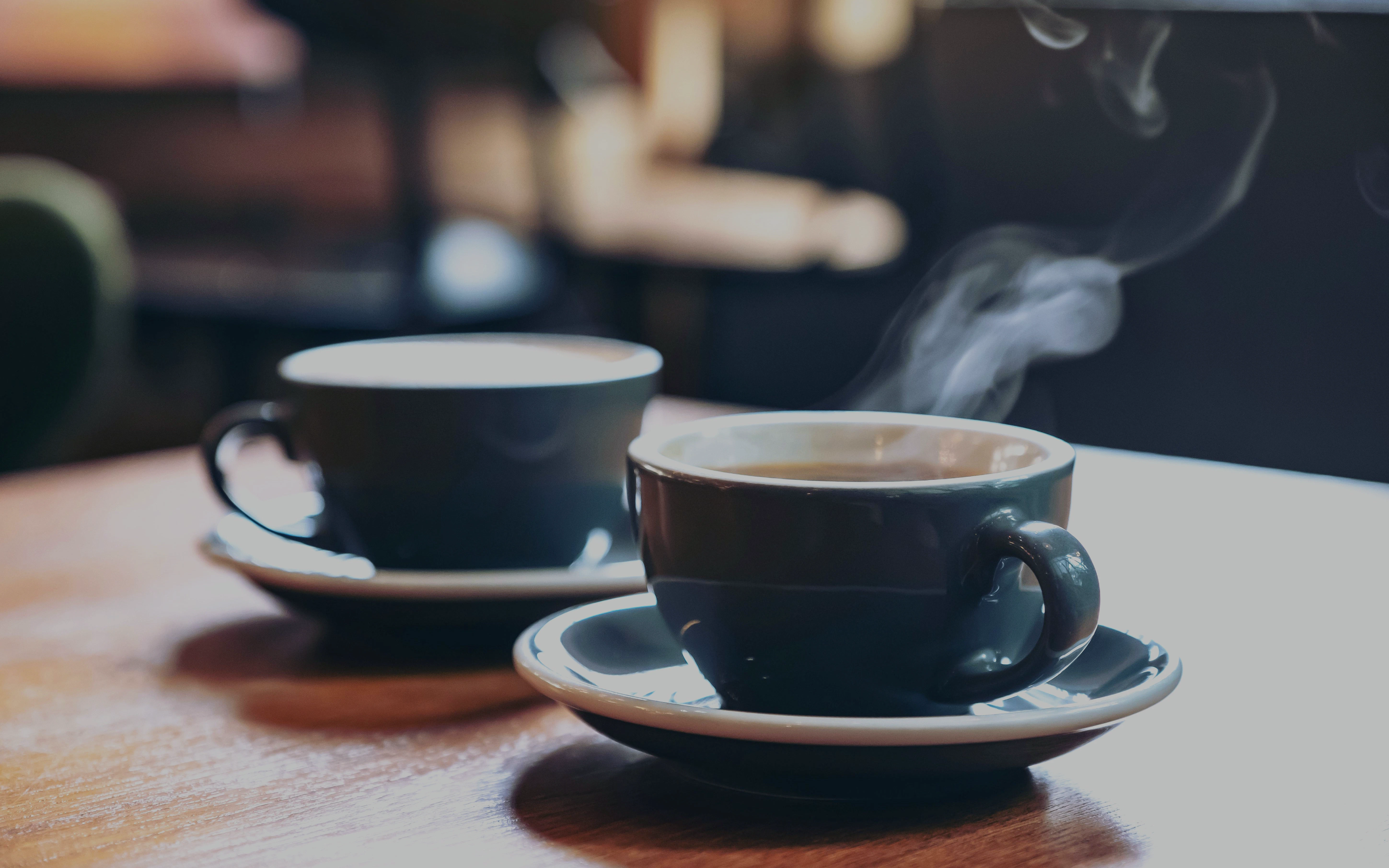Two blue cups of steaming latte and Americano on a wooden table in a cafe.