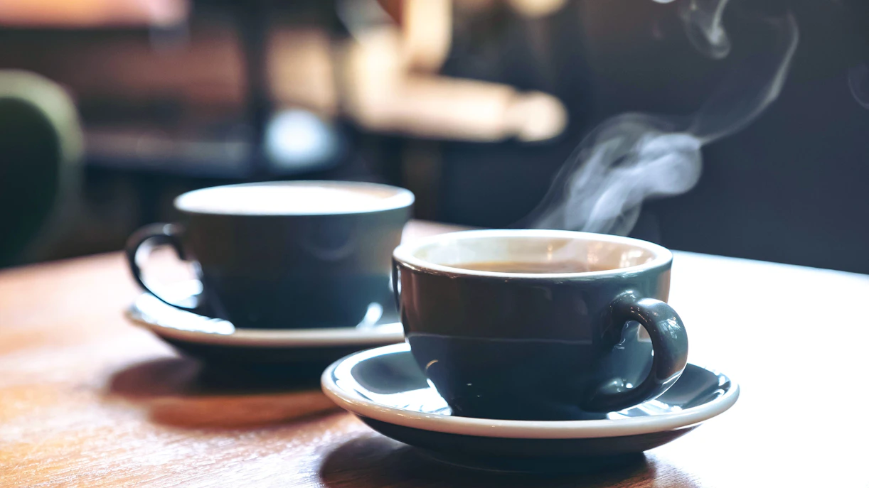 Two blue cups of steaming latte and Americano on a wooden table in a cafe.