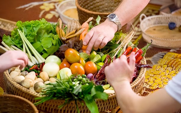 Hands selecting fresh vegetables and herbs at Silom Thai Cooking School.