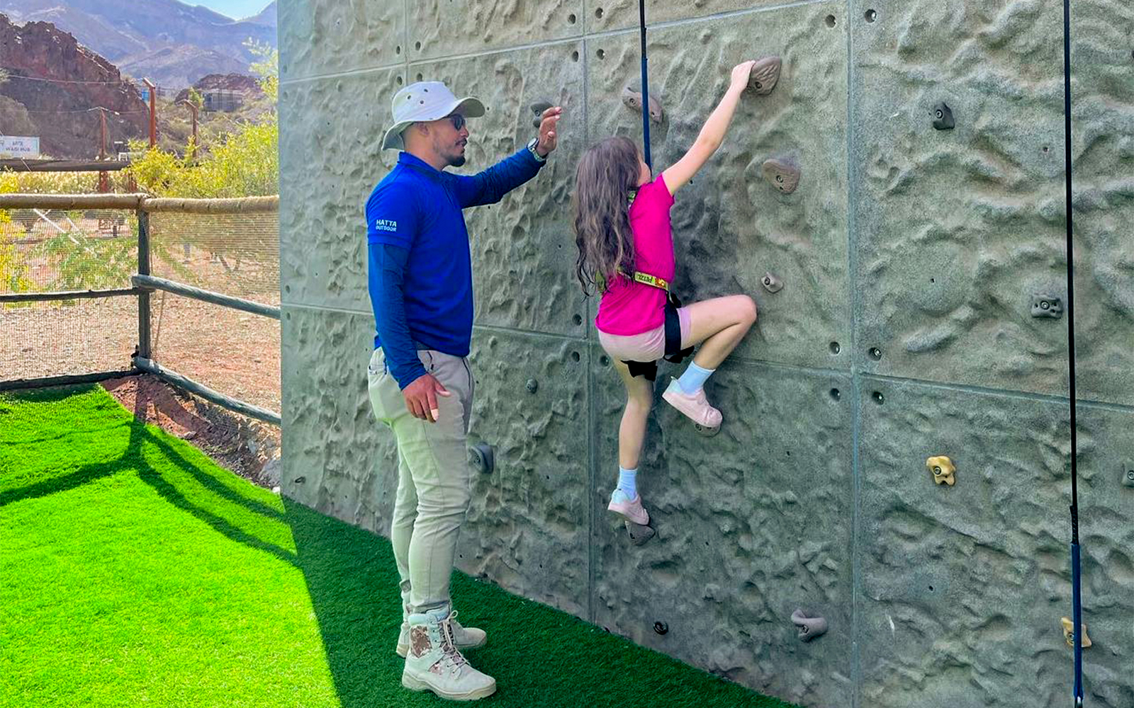 Kid climbing an indoor wall with guide's assistance in adventure center.