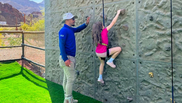 Kid climbing an indoor wall with guide's assistance in adventure center.