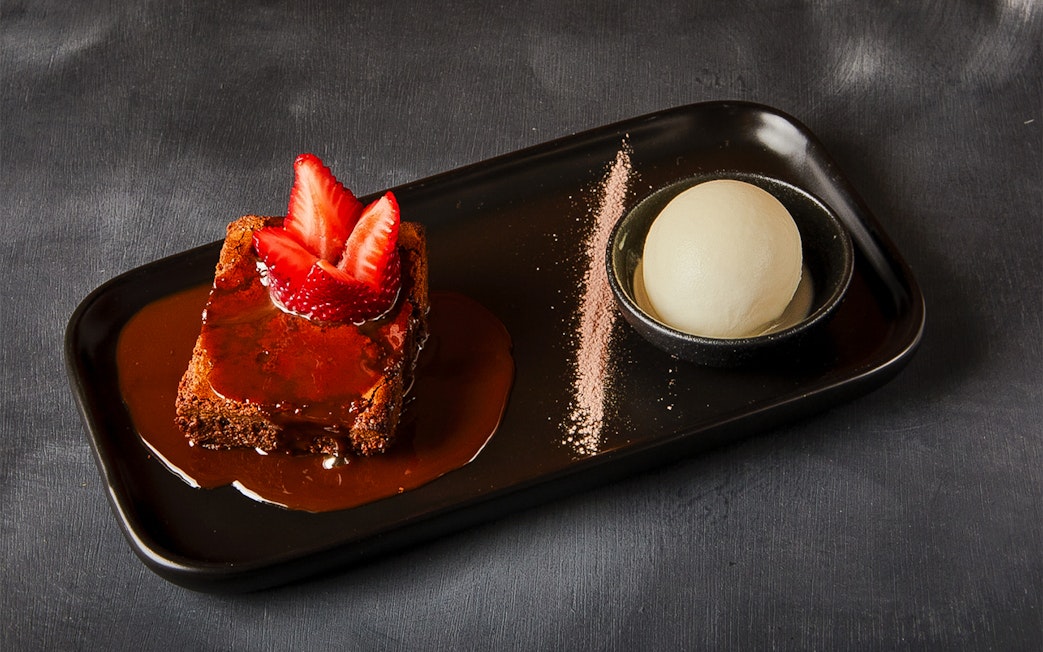 Chocolate cake topped with strawberries and a scoop of ice cream on a black plate.