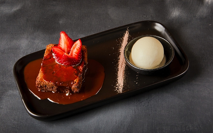 Chocolate cake topped with strawberries and a scoop of ice cream on a black plate.