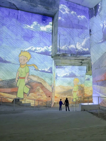 Little Prince projections at Carrières des Lumières exhibition, featuring visitors exploring the illuminated quarry.