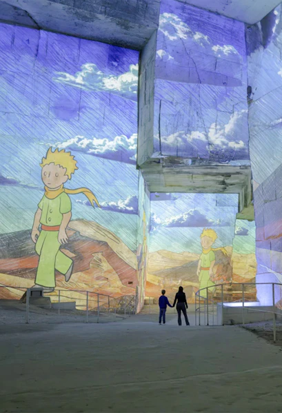 Little Prince projections at Carrières des Lumières exhibition, featuring visitors exploring the illuminated quarry.