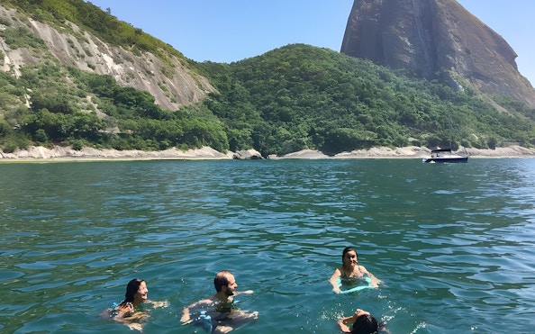Tourists swimming in Rio de Janeiro waters with Sugarloaf Mountain in the background.