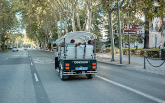 Tourists on an electric tuk-tuk tour in Madrid, passing by Museo del Prado signs.
