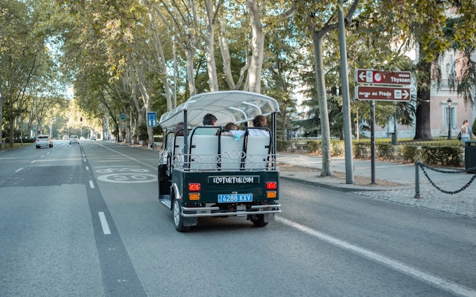 Tourists on an electric tuk-tuk tour in Madrid, passing by Museo del Prado signs.