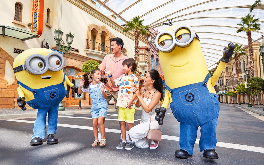 Family interacting with Minion characters at Universal Studios Singapore entrance.