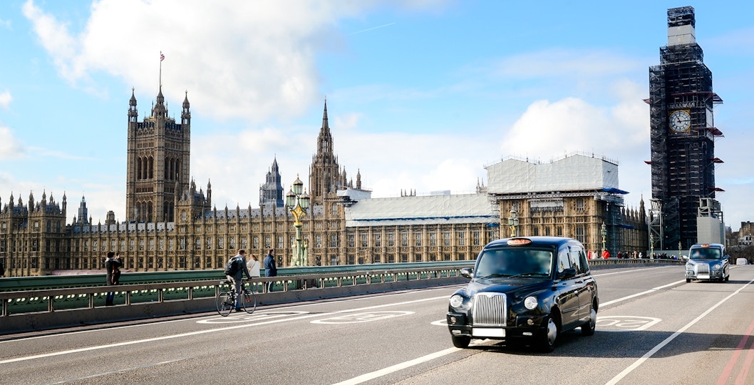 Black cabs drive on Westminster Bridge with Big Ben and Houses of Parliament in London.