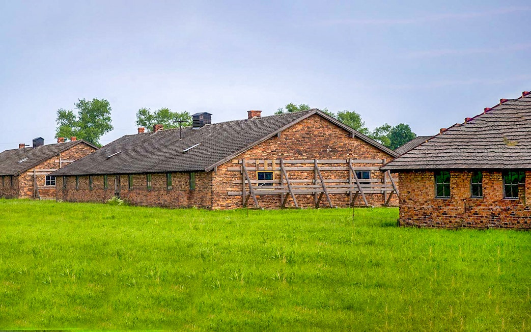 Brick barracks at Auschwitz-Birkenau Museum, Poland, surrounded by green grass.