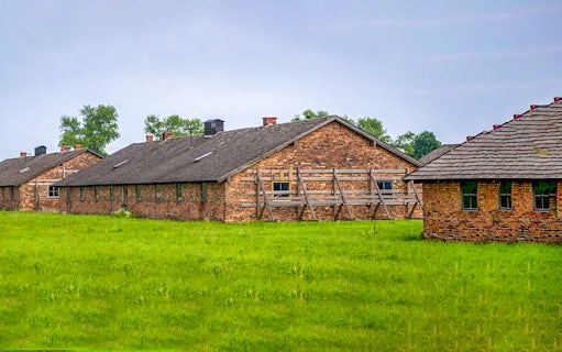 Brick barracks at Auschwitz-Birkenau Museum, Poland, surrounded by green grass.