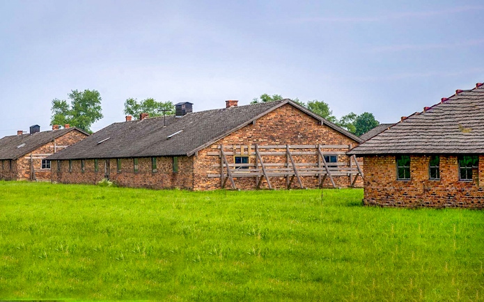 Brick barracks at Auschwitz-Birkenau Museum, Poland, surrounded by green grass.