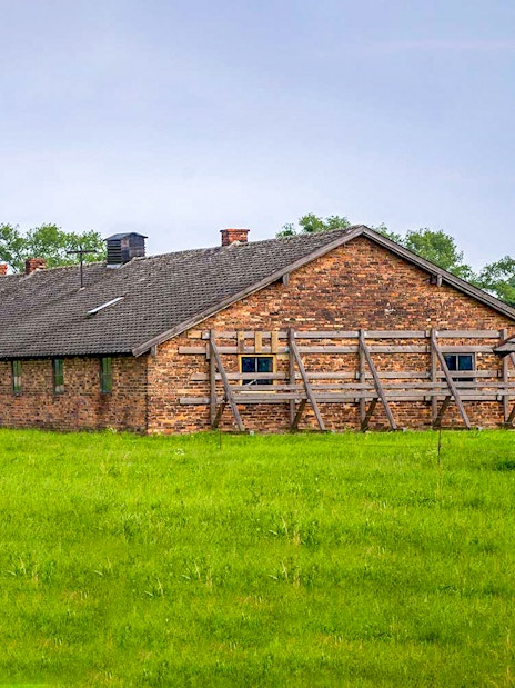 Brick barracks at Auschwitz-Birkenau Museum, Poland, surrounded by green grass.