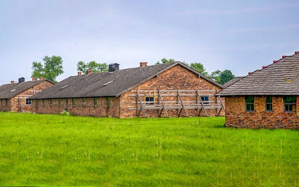 Brick barracks at Auschwitz-Birkenau Museum, Poland, surrounded by green grass.