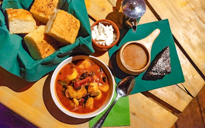 Traditional Alaskan meal with stew, bread, and dessert in a Gamme hut setting.