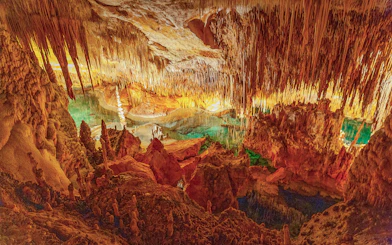 Stalactites and stalagmites in the illuminated Caves of Drach, Mallorca, with turquoise water.