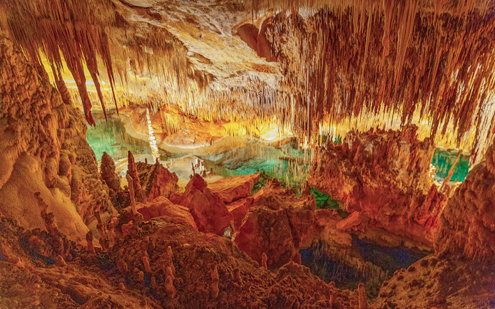 Stalactites and stalagmites in the illuminated Caves of Drach, Mallorca, with turquoise water.