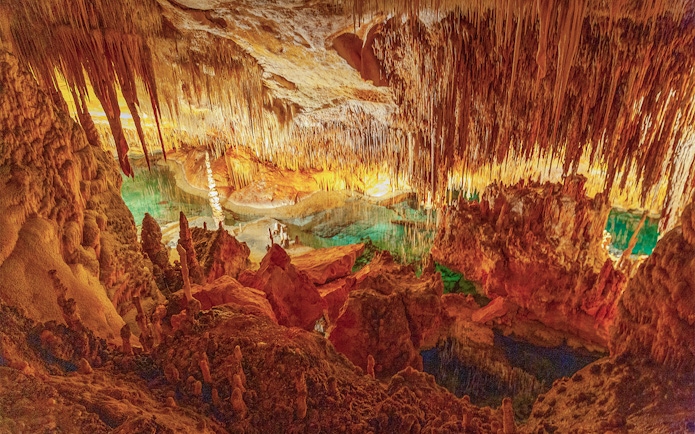 Stalactites and stalagmites in the illuminated Caves of Drach, Mallorca, with turquoise water.