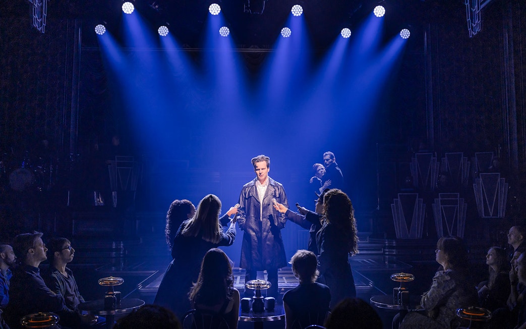 Performer on stage under blue lights with audience in a theater setting.