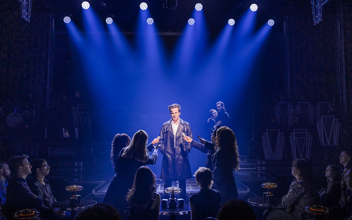 Performer on stage under blue lights with audience in a theater setting.
