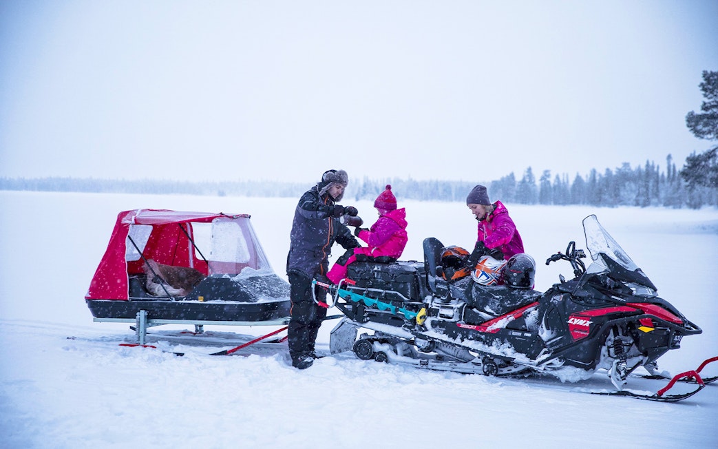 Snowmobile tour group in snowy landscape preparing for Northern Lights excursion.