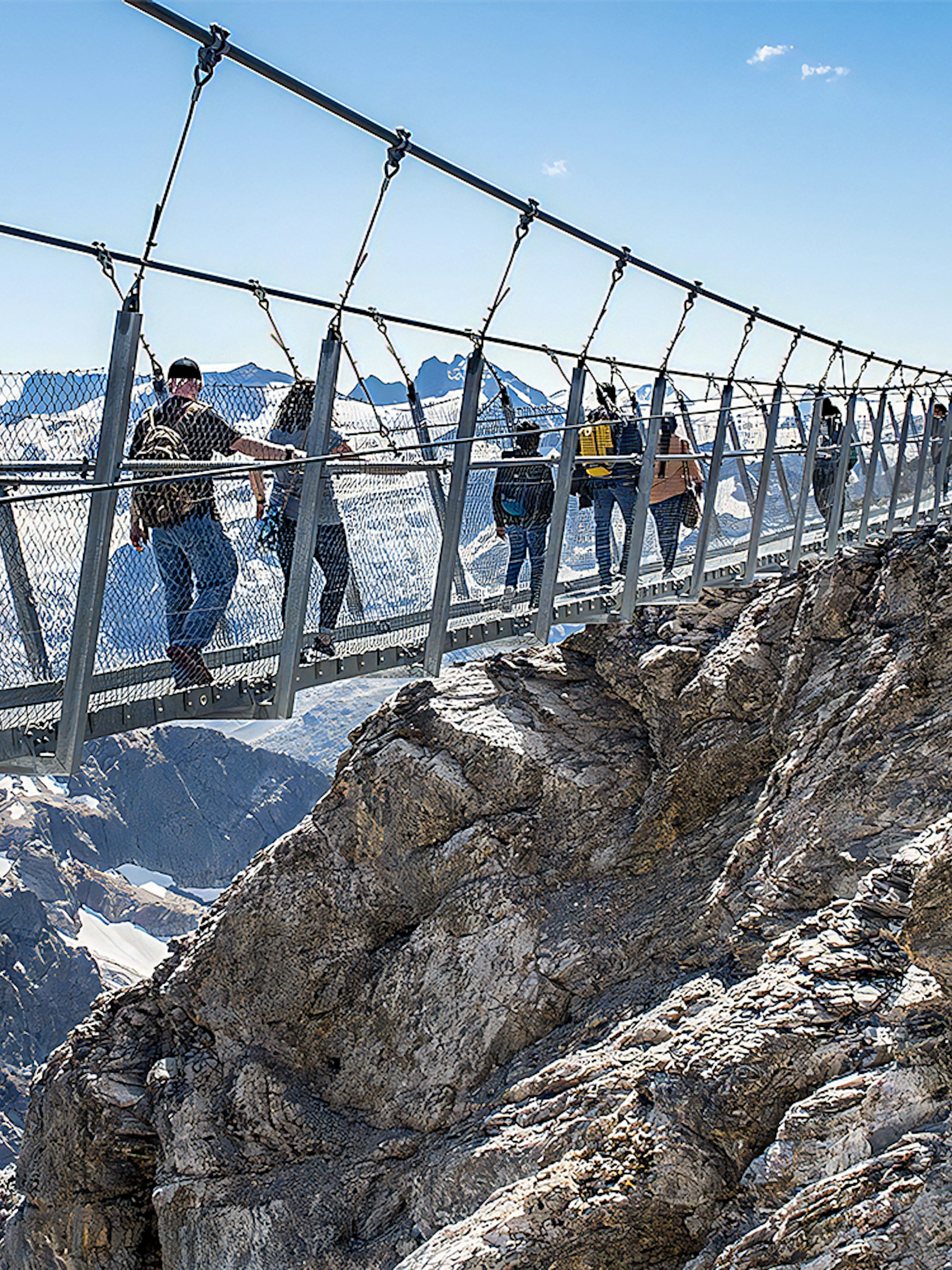 Tourists crossing a suspension bridge at Mt. Titlis with snowy peaks in the background.