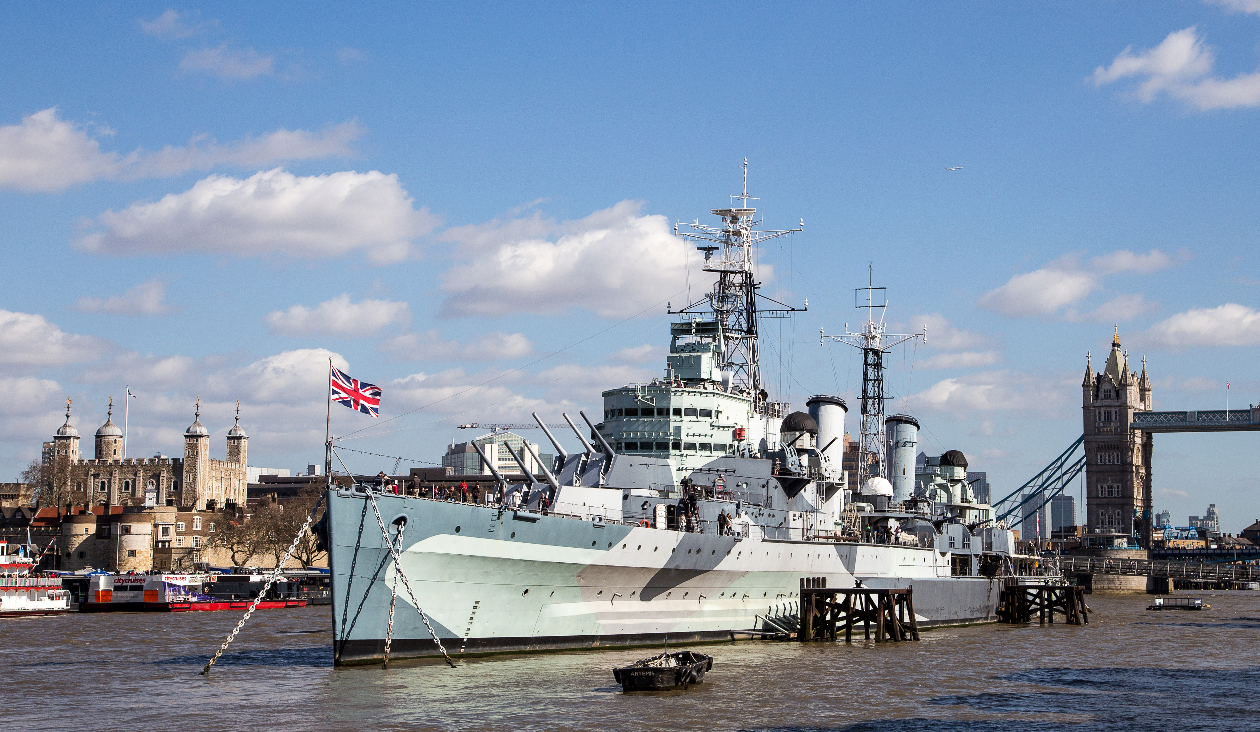 HMS Belfast moored on the River Thames with Tower Bridge and the Tower of London in the background.