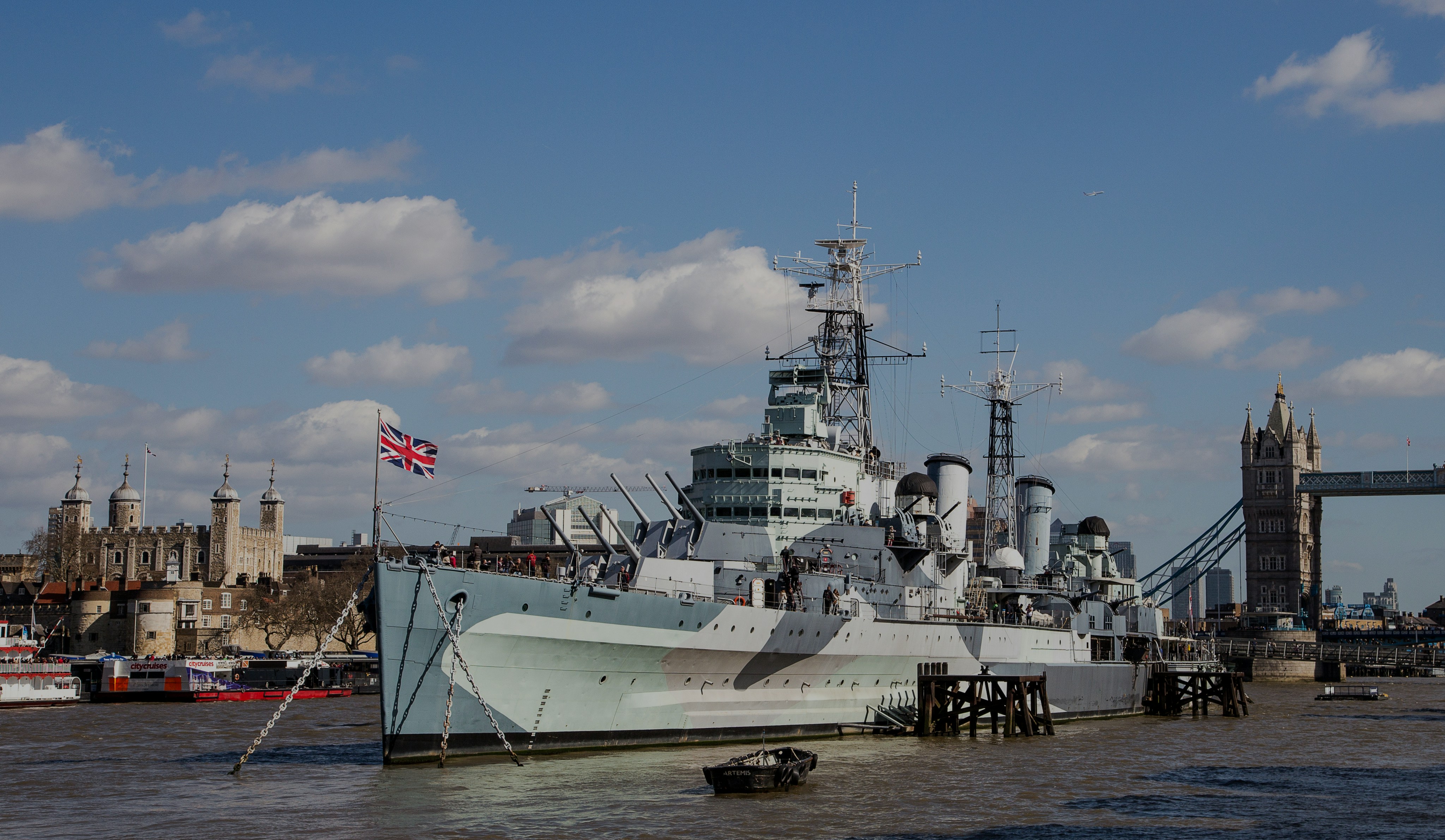 HMS Belfast moored on the River Thames with Tower Bridge and the Tower of London in the background.