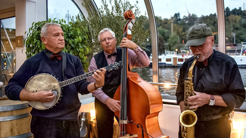 Musicians playing banjo, double bass, and saxophone on a Prague dinner cruise with live music.