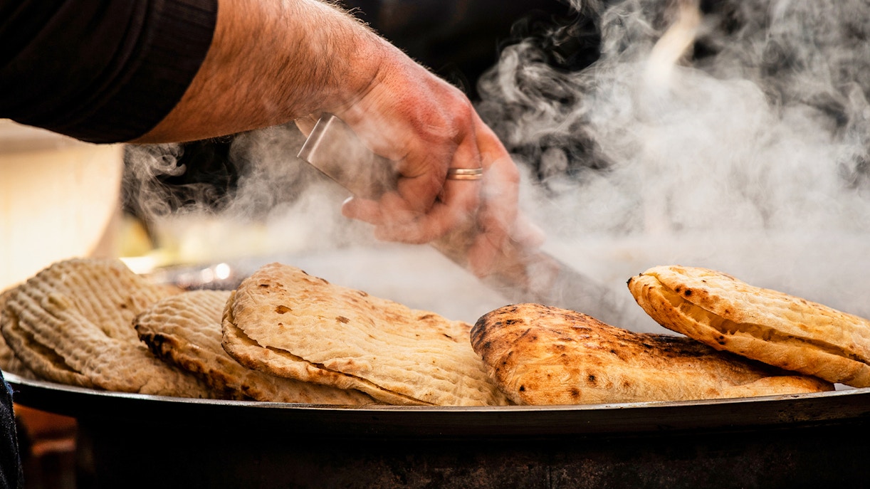 Freshly baked flatbreads steaming on a grill during a food tour in Milan.