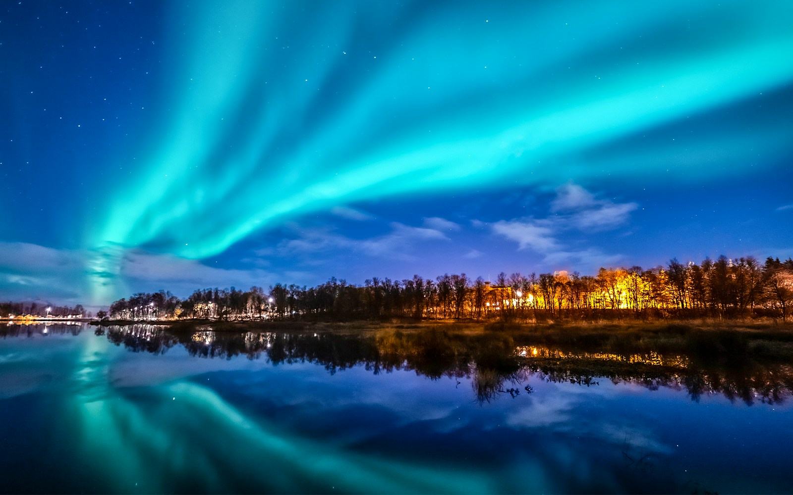 Northern Lights over a forest and lake in Norway.