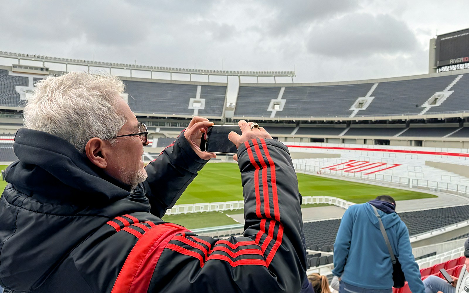 Tourist taking photos at La Bombonera stadium, Buenos Aires, capturing iconic blue and yellow stands.