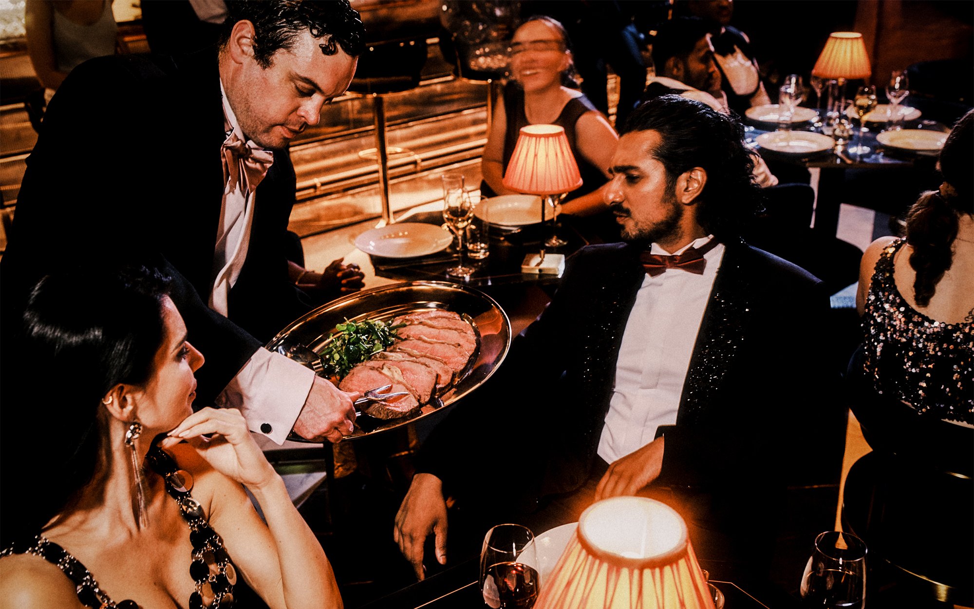 Server presenting a platter of sliced meat to diners at a 58th Street performance venue.