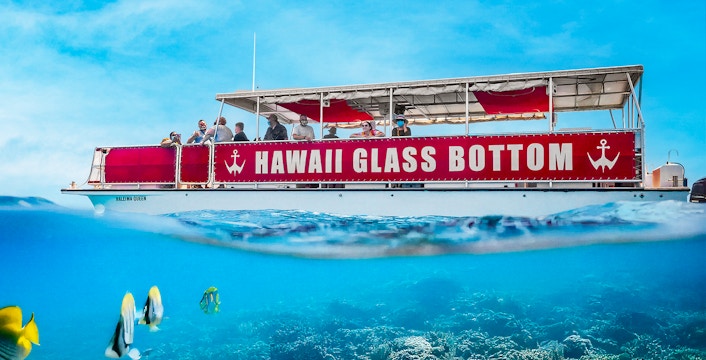 Hawaii glass bottom boat with passengers sailing over coral reef.