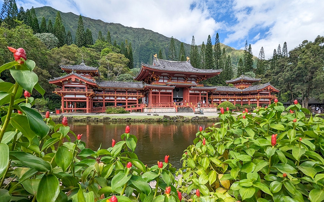 Byodo-In Temple in Oahu, Hawaii with lush greenery and pond in foreground.