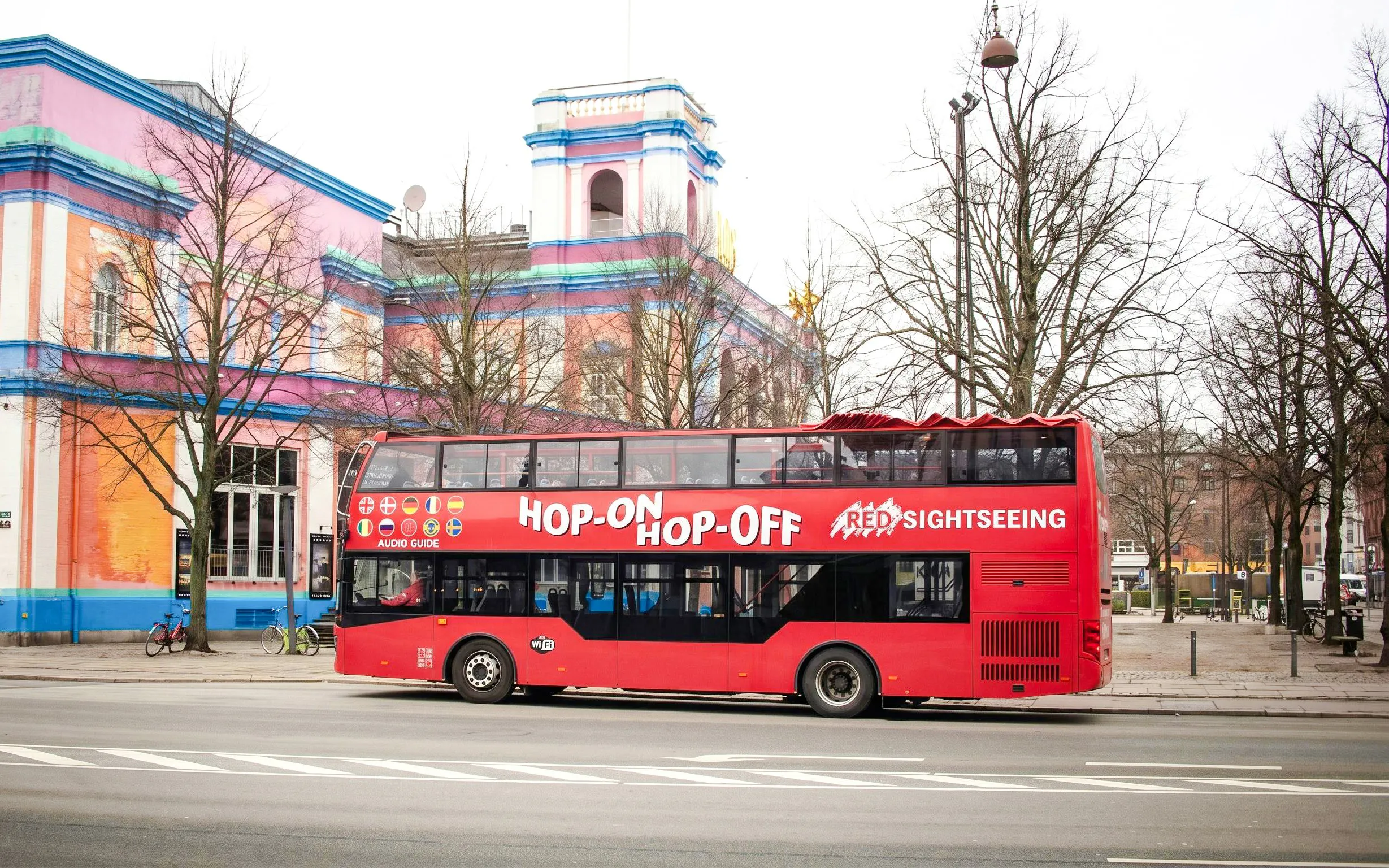 Red Sightseeing Copenhagen hop-on hop-off bus near colorful building.