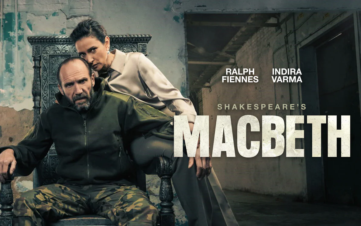 Actors in a dramatic scene from Shakespeare's Macbeth, with a rustic backdrop.