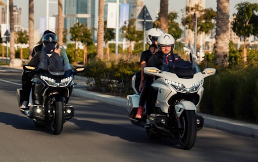 Two motorcycles with passengers riding through a palm-lined street in Dubai.