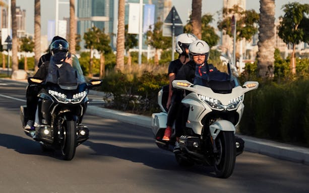 Two motorcycles with passengers riding through a palm-lined street in Dubai.