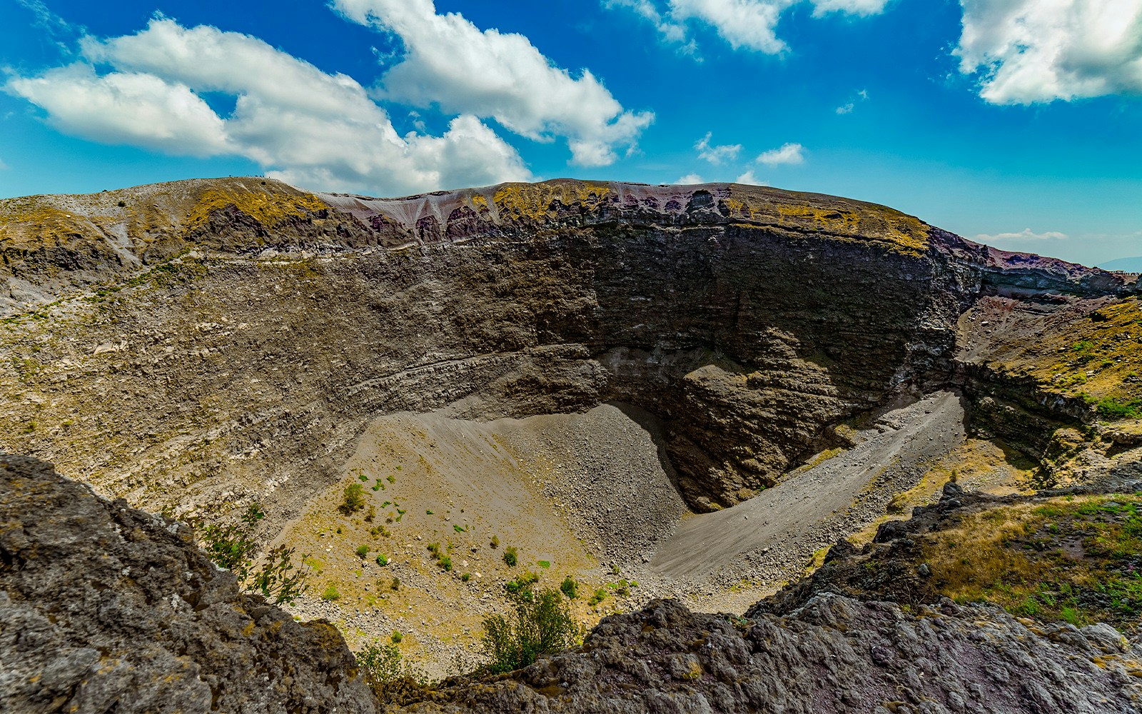 Crater of Monte Vesuvio under a blue sky, showcasing rugged volcanic terrain.
