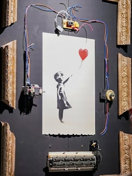 Banksy's "Girl with Red Balloon" artwork with mechanical frame at Banksy Limitless exhibit.