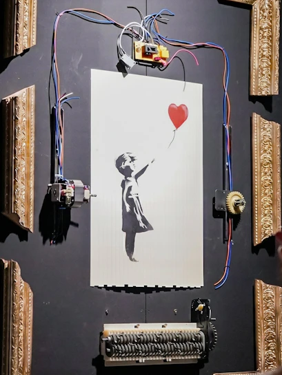Banksy's "Girl with Red Balloon" artwork with mechanical frame at Banksy Limitless exhibit.