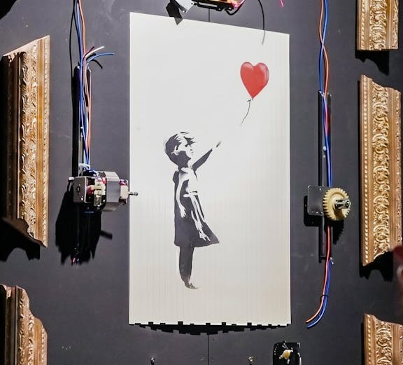 Banksy's "Girl with Red Balloon" artwork with mechanical frame at Banksy Limitless exhibit.